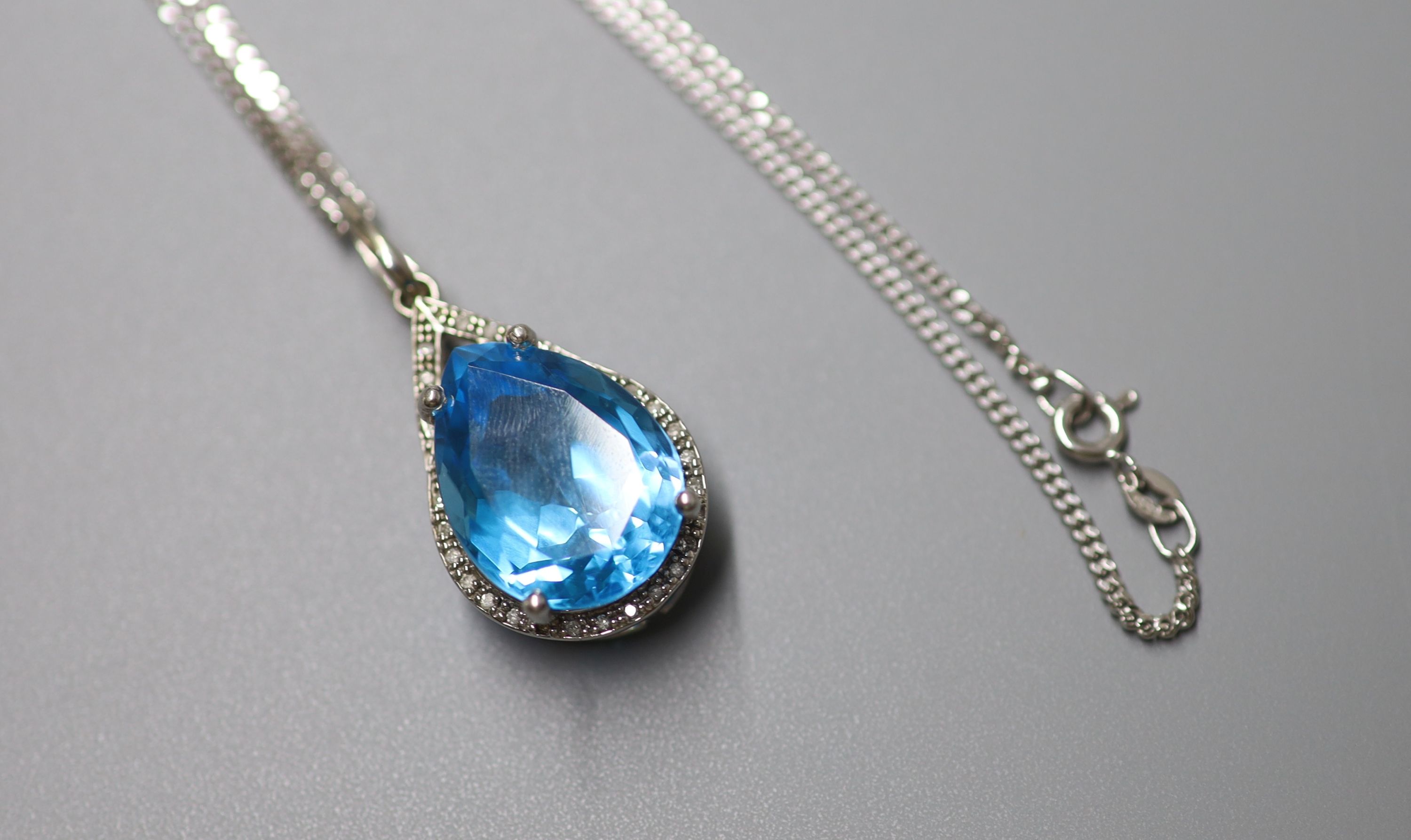 A modern white metal (stamped 9k), blue topaz and diamond chip set pendant, 29mm, on a 9ct white gold chain, 44cm, gross weight 12.3 grams